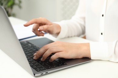 Photo of Businesswoman using laptop at white table indoors, closeup. Modern technology