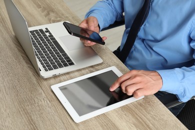 Photo of Businessman with smartphone, tablet and laptop at wooden table, closeup. Modern technology