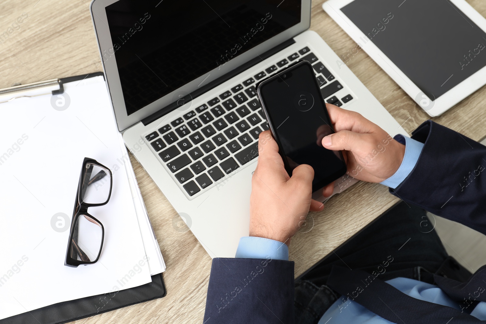 Photo of Businessman using smartphone near laptop at wooden table, closeup. Modern technology