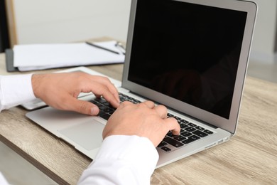 Photo of Businessman using laptop at wooden table, closeup. Modern technology