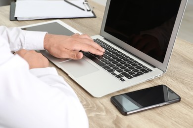 Photo of Businessman using laptop at wooden table, closeup. Modern technology