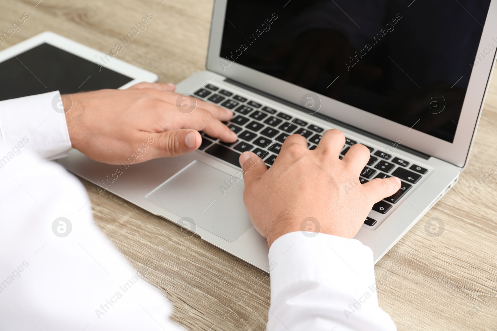 Photo of Businessman using laptop at wooden table, closeup. Modern technology