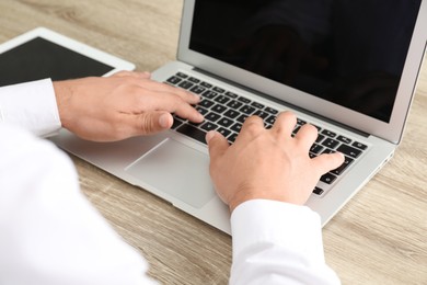 Photo of Businessman using laptop at wooden table, closeup. Modern technology