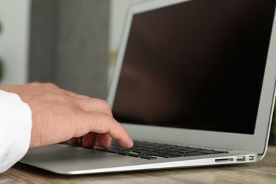 Photo of Businessman using laptop at wooden table, closeup. Modern technology