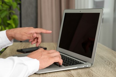 Photo of Businessman using laptop at wooden table, closeup. Modern technology