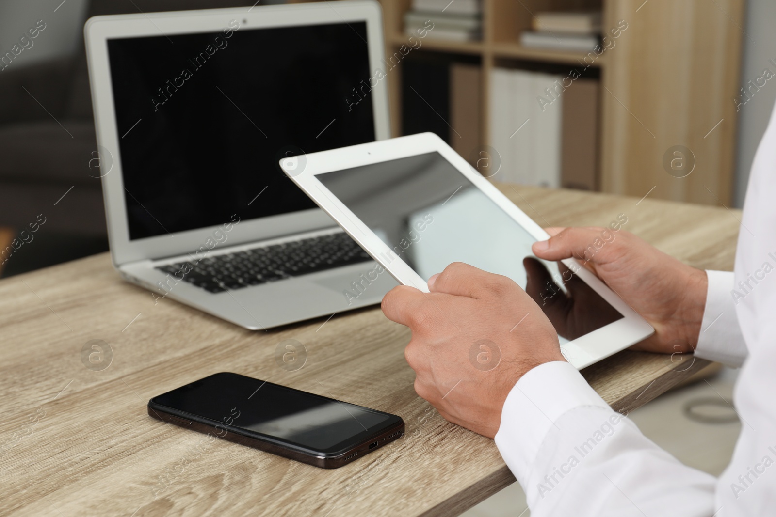 Photo of Businessman with tablet, smartphone and laptop at wooden table, closeup. Modern technology