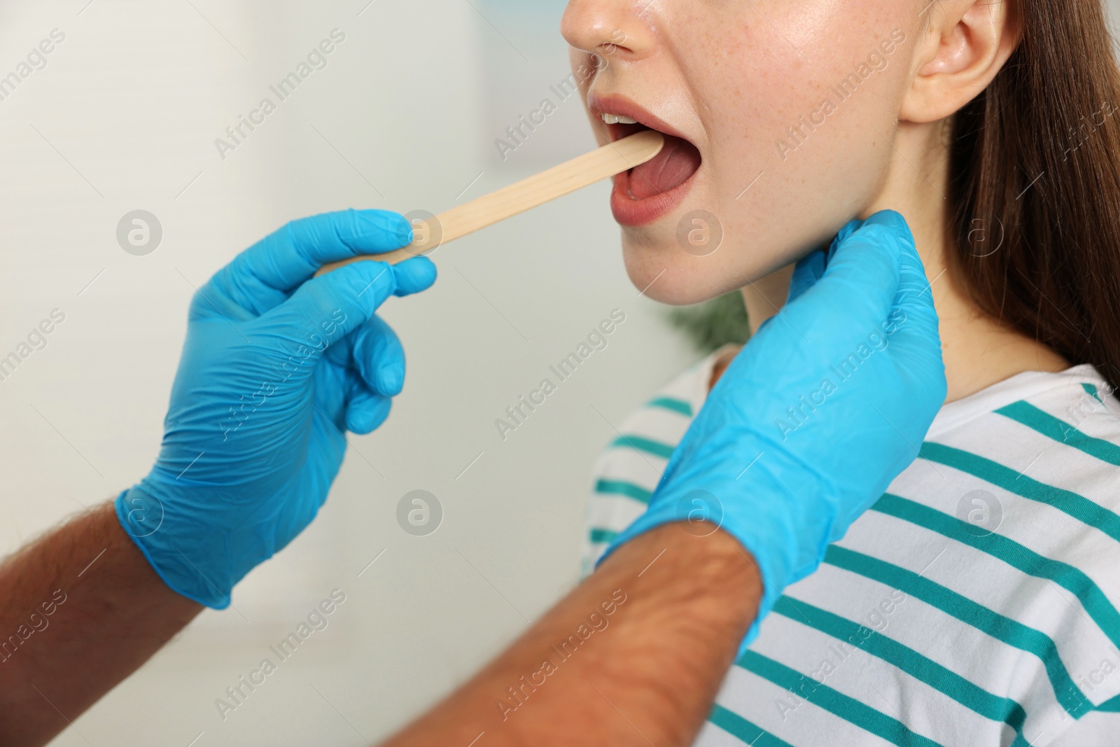 Photo of Doctor examining woman's throat with tongue depressor in clinic, closeup