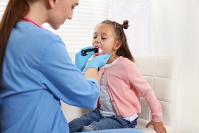 Photo of Doctor examining girl's throat with flashlight in clinic