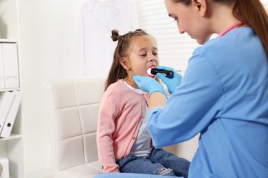 Photo of Doctor examining girl's throat with flashlight in clinic