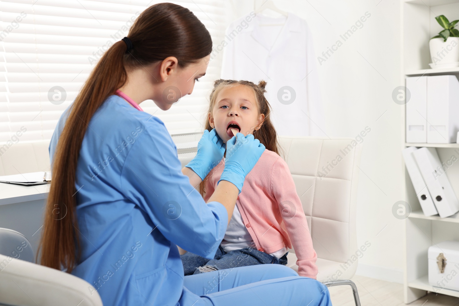 Photo of Doctor examining girl's throat with tongue depressor in clinic