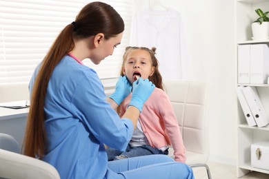 Photo of Doctor examining girl's throat with tongue depressor in clinic