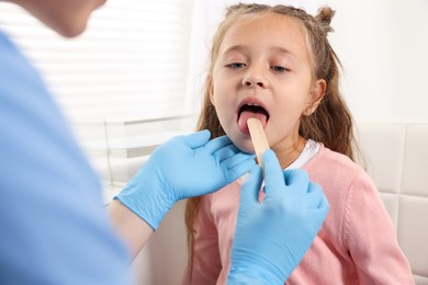 Photo of Doctor examining girl's throat with tongue depressor in clinic