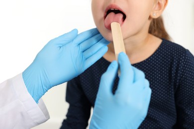 Doctor examining girl's throat with tongue depressor in clinic, closeup