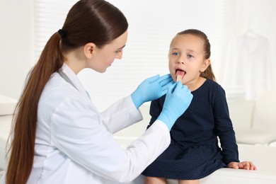 Photo of Doctor examining girl's throat with tongue depressor in clinic