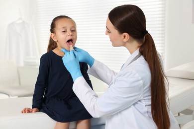 Photo of Doctor examining girl's throat with tongue depressor in clinic