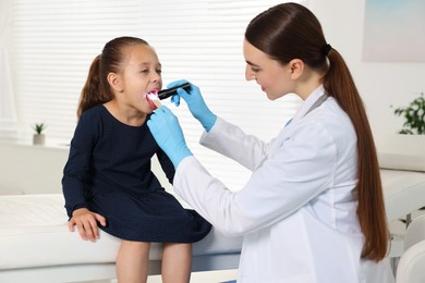 Photo of Doctor examining girl's throat with flashlight and tongue depressor in clinic