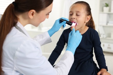 Photo of Doctor examining girl's throat with flashlight and tongue depressor in clinic