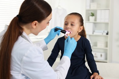 Photo of Doctor examining girl's throat with flashlight and tongue depressor in clinic