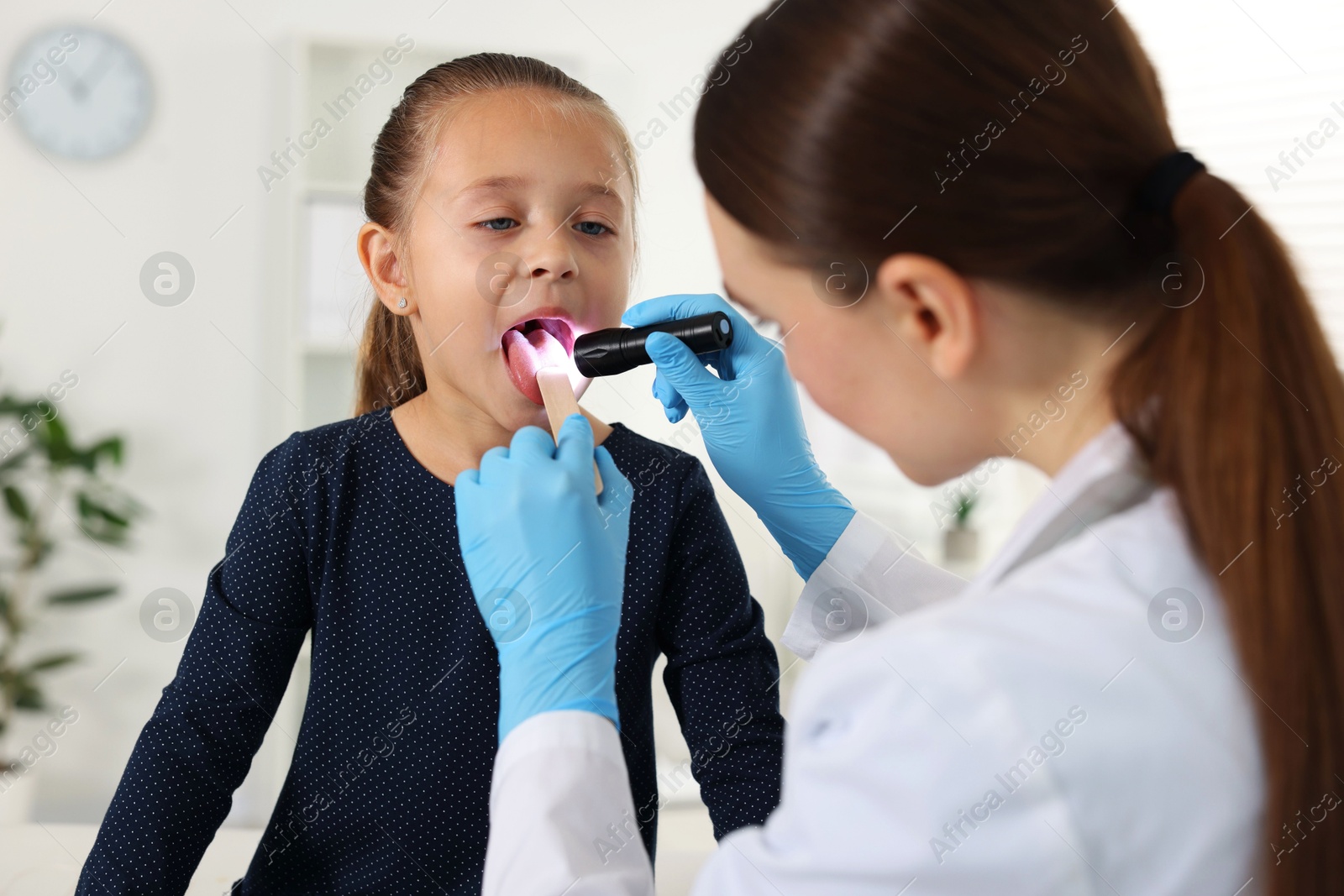 Photo of Doctor examining girl's throat with flashlight and tongue depressor in clinic