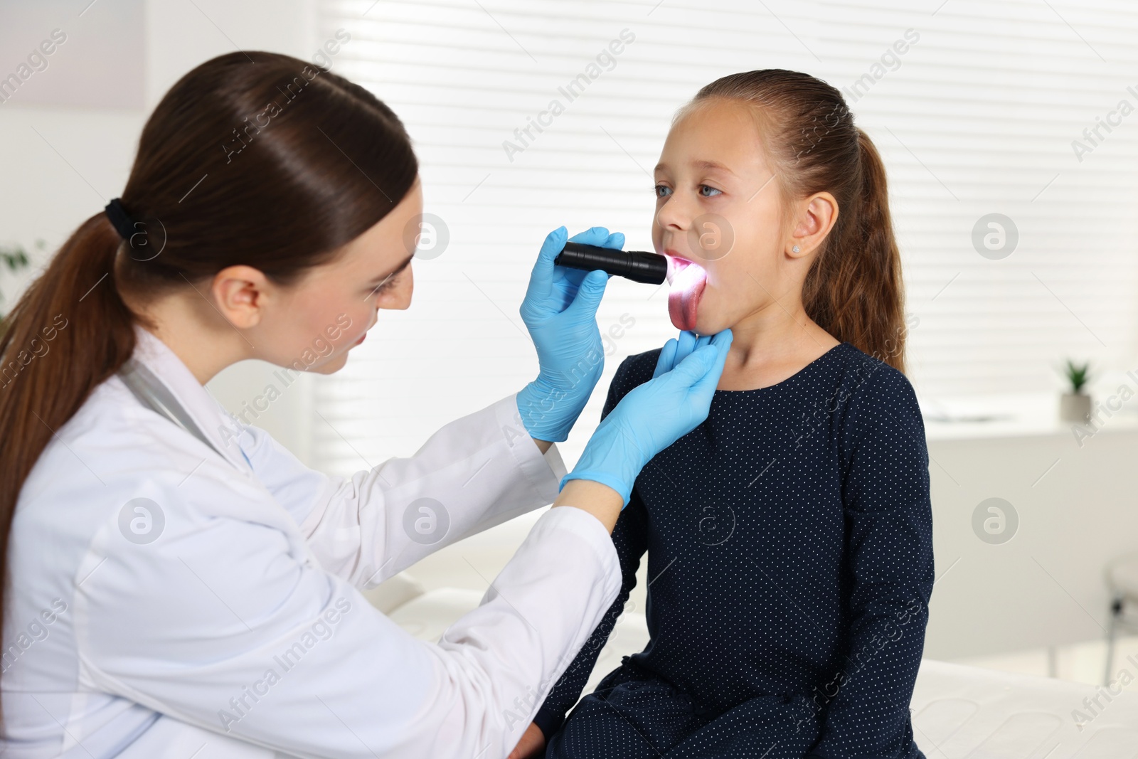 Photo of Doctor examining girl's throat with flashlight in clinic