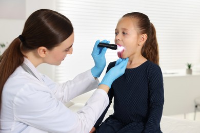 Doctor examining girl's throat with flashlight in clinic