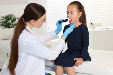 Doctor examining girl's throat with flashlight in clinic