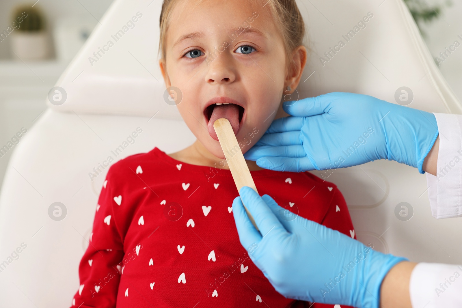 Photo of Doctor examining girl's throat with tongue depressor in clinic