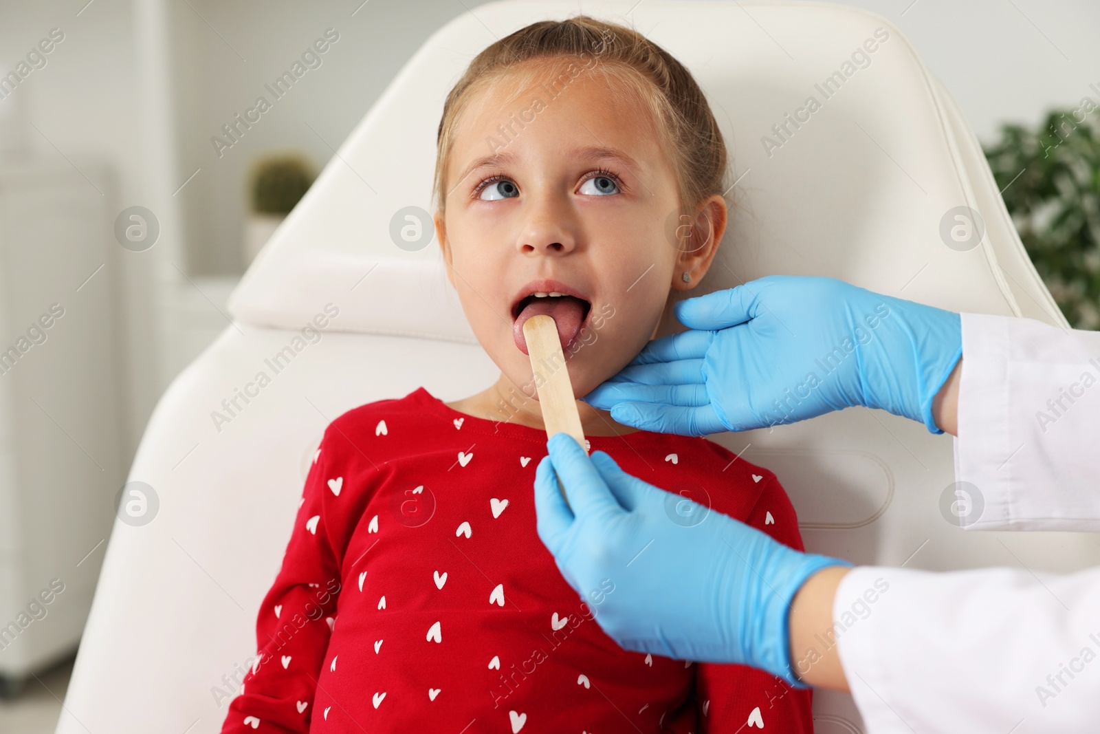 Photo of Doctor examining girl's throat with tongue depressor in clinic