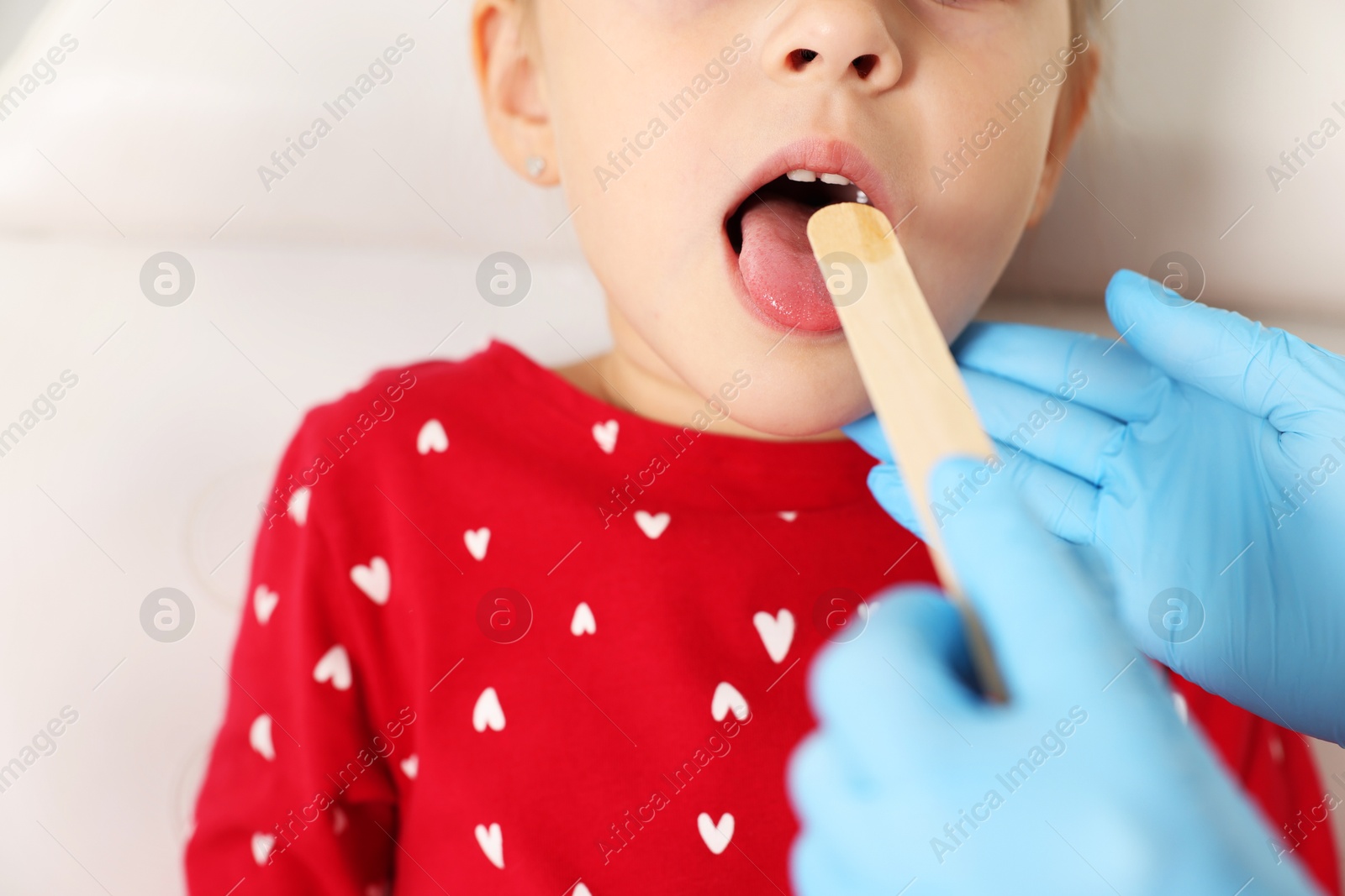 Photo of Doctor examining girl's throat with tongue depressor in clinic, closeup