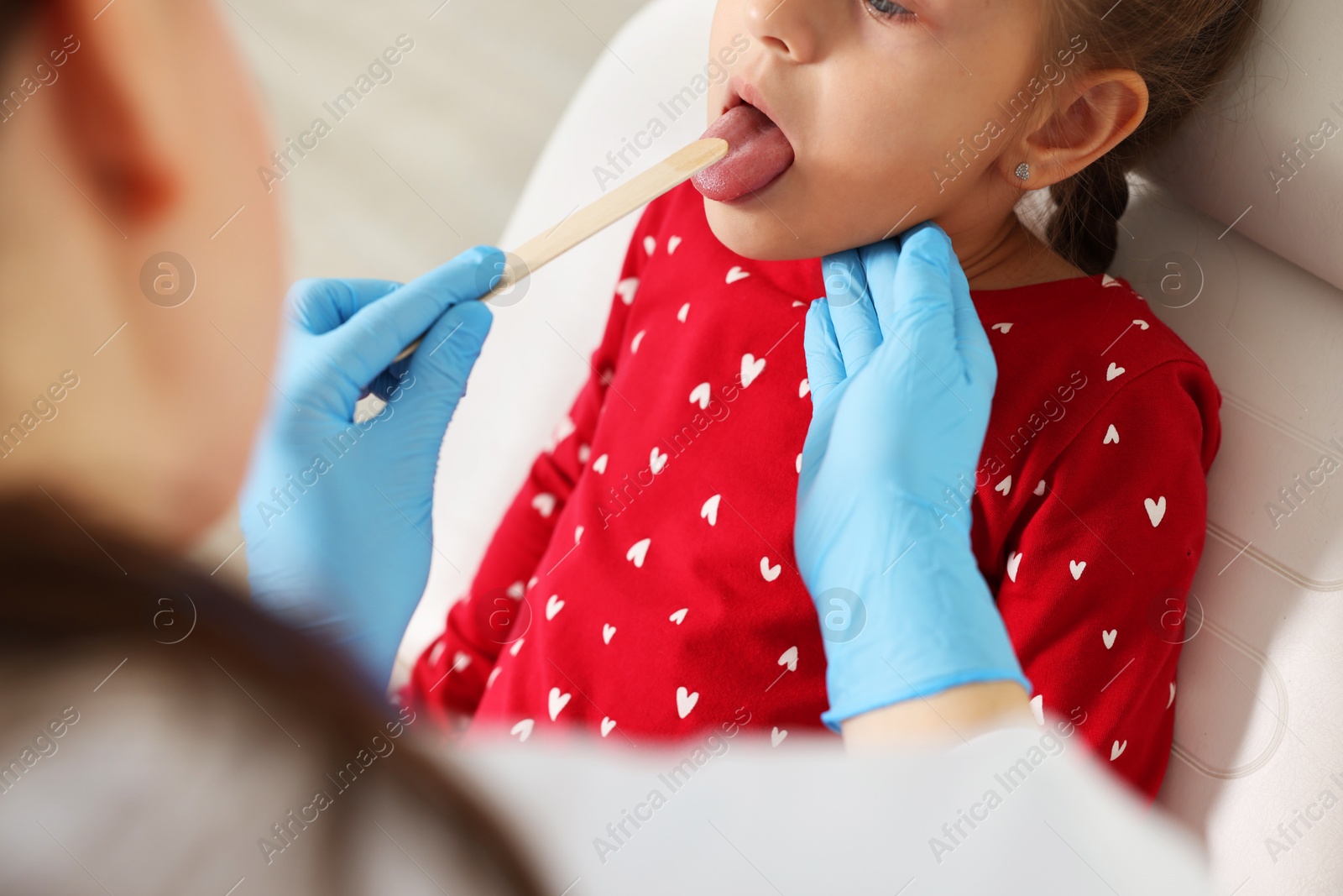 Photo of Doctor examining girl's throat with tongue depressor in clinic