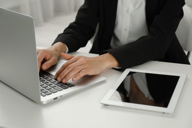 Photo of Businesswoman using laptop at white table indoors, closeup. Modern technology