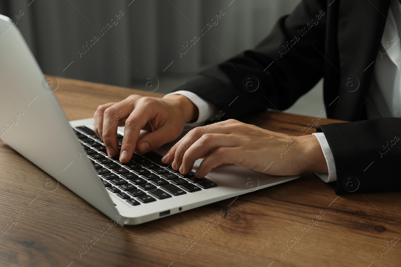 Photo of Businesswoman using laptop at wooden table indoors, closeup. Modern technology