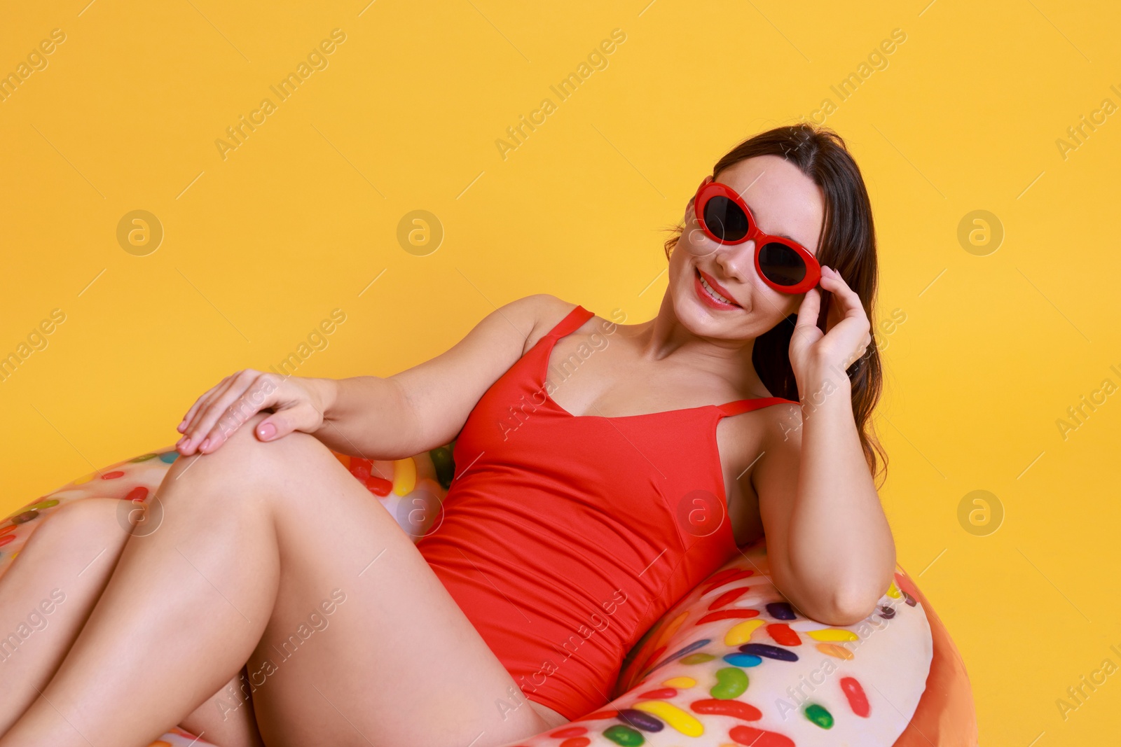 Photo of Beautiful woman in swimsuit with inflatable ring on yellow background