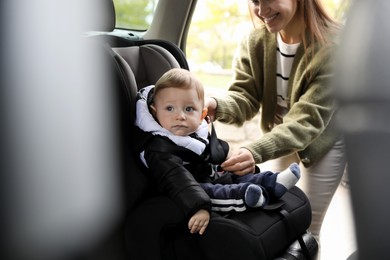 Photo of Smiling mother fastening her baby in car seat, closeup