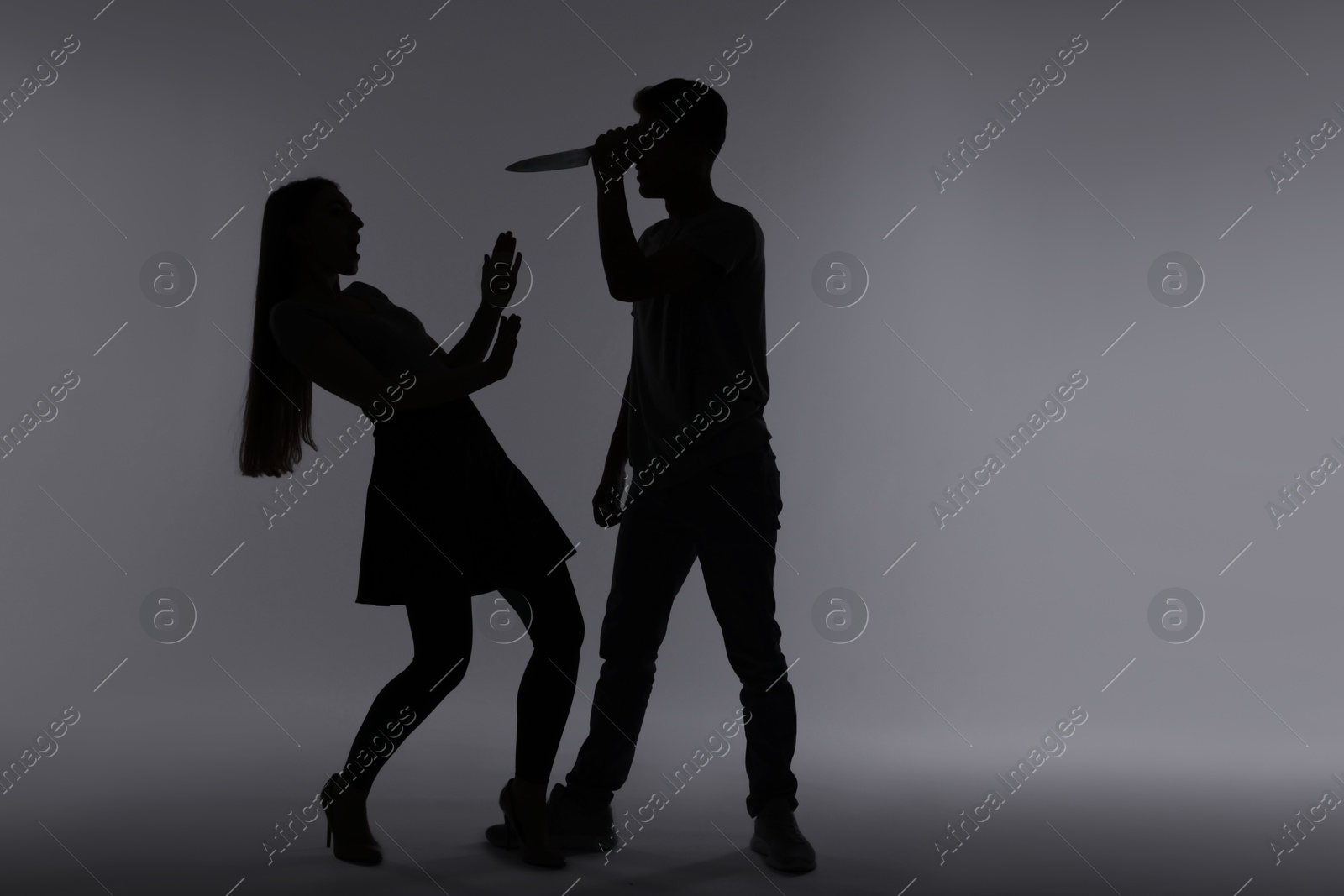 Photo of Domestic violence. Silhouette of man with knife threatening his wife on grey background