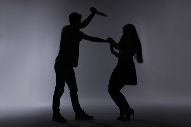 Photo of Domestic violence. Silhouette of man with knife threatening his wife on grey background