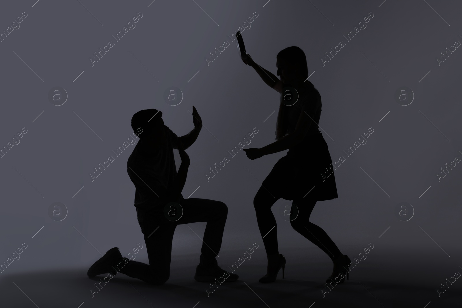 Photo of Domestic violence. Silhouette of woman with frying pan threatening her husband on grey background