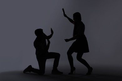 Photo of Domestic violence. Silhouette of woman with frying pan threatening her husband on grey background