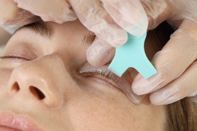 Photo of Eyelash lamination procedure. Esthetician applying adhesive on woman's lashes in beauty salon, closeup