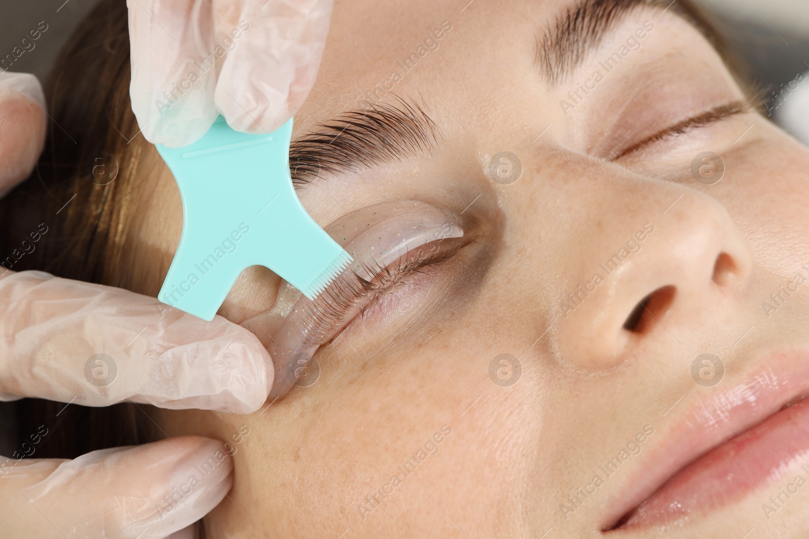 Photo of Eyelash lamination procedure. Esthetician applying adhesive on woman's lashes in beauty salon, closeup