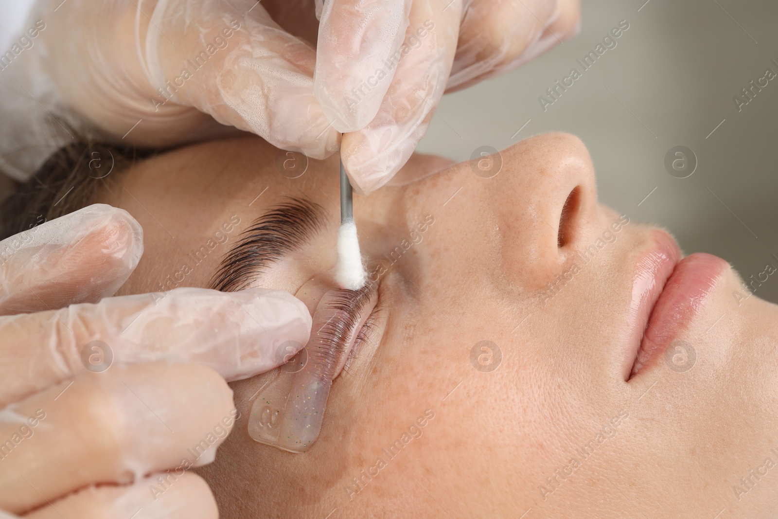 Photo of Eyelash lamination procedure. Esthetician smoothing woman's lashes on pad in beauty salon, closeup