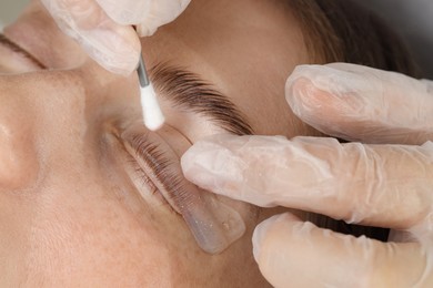 Eyelash lamination procedure. Esthetician smoothing woman's lashes on pad in beauty salon, closeup