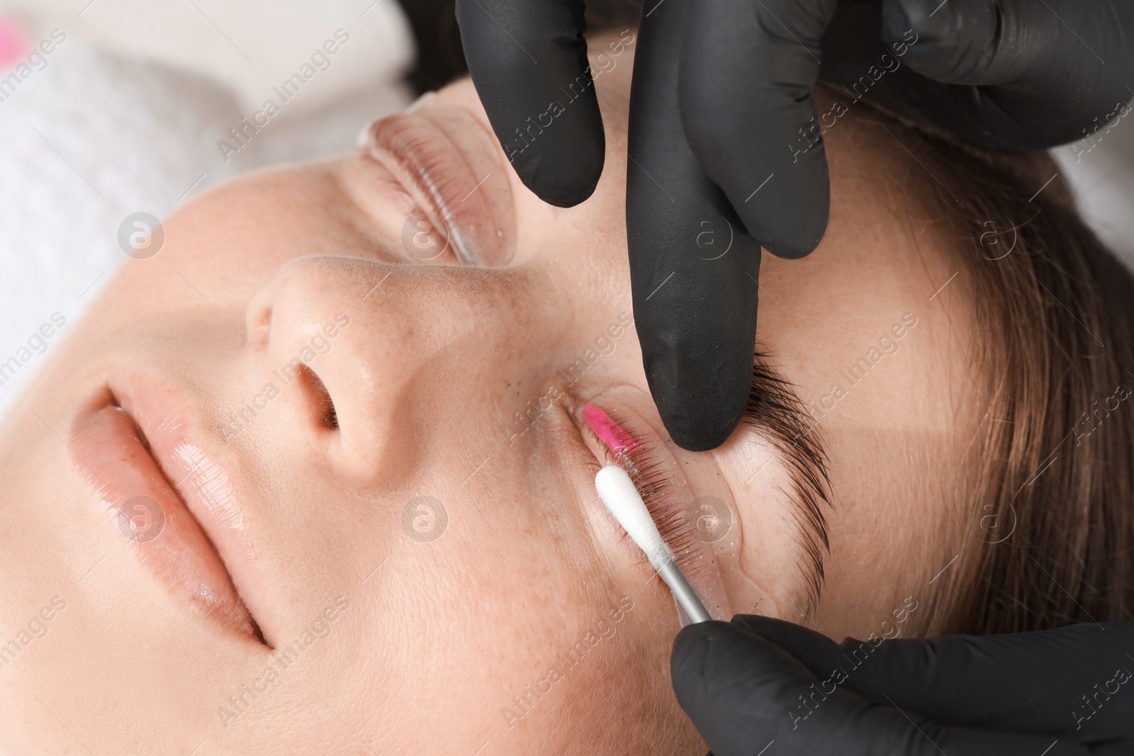 Photo of Eyelash lamination procedure. Esthetician wiping lotion from woman's lashes in beauty salon, closeup