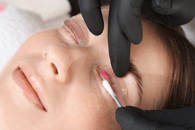 Photo of Eyelash lamination procedure. Esthetician wiping lotion from woman's lashes in beauty salon, closeup