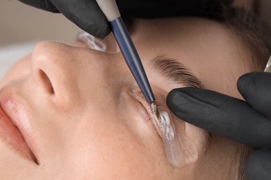 Eyelash lamination procedure. Esthetician applying lotion on woman's lashes in beauty salon, closeup