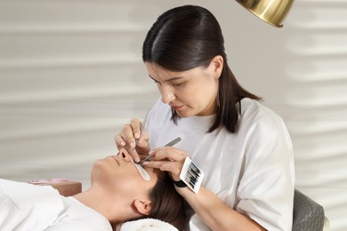 Photo of Esthetician applying lash extensions on natural ones in beauty salon