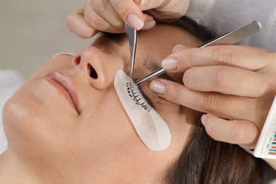 Photo of Woman undergoing lash extensions procedure in beauty salon, closeup