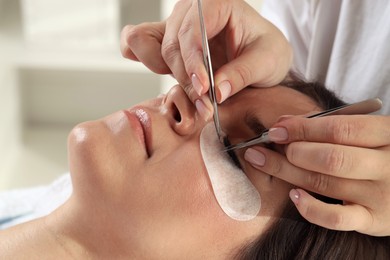 Photo of Woman undergoing lash extensions procedure in beauty salon, closeup