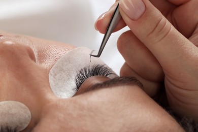 Photo of Woman undergoing lash extensions procedure in beauty salon, closeup