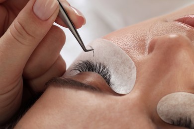 Photo of Woman undergoing lash extensions procedure in beauty salon, closeup